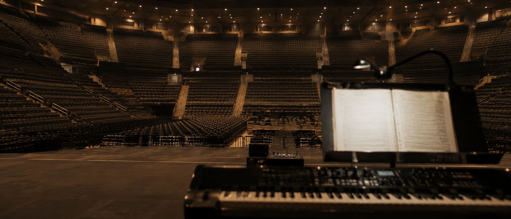 View from behind a music director's keyboard rig looking out at an empty arena
